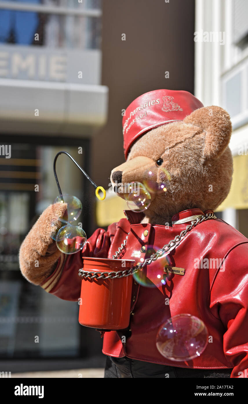 Grande orso di peluche con Red Hat e giacca di pelle soffia bolle di sapone in aria Foto Stock