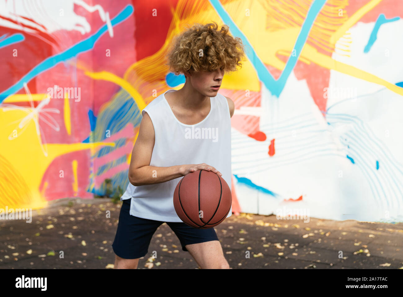 Gli uomini con la curva dei capelli e t-shirt bianco giocare a basket fuori in una corte con graffiti Foto Stock