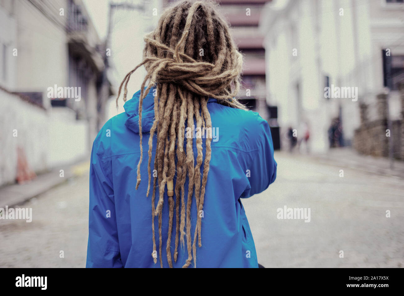 Giovane uomo per le strade con lunghi dreadlocks utilizzando giacca blu Foto Stock