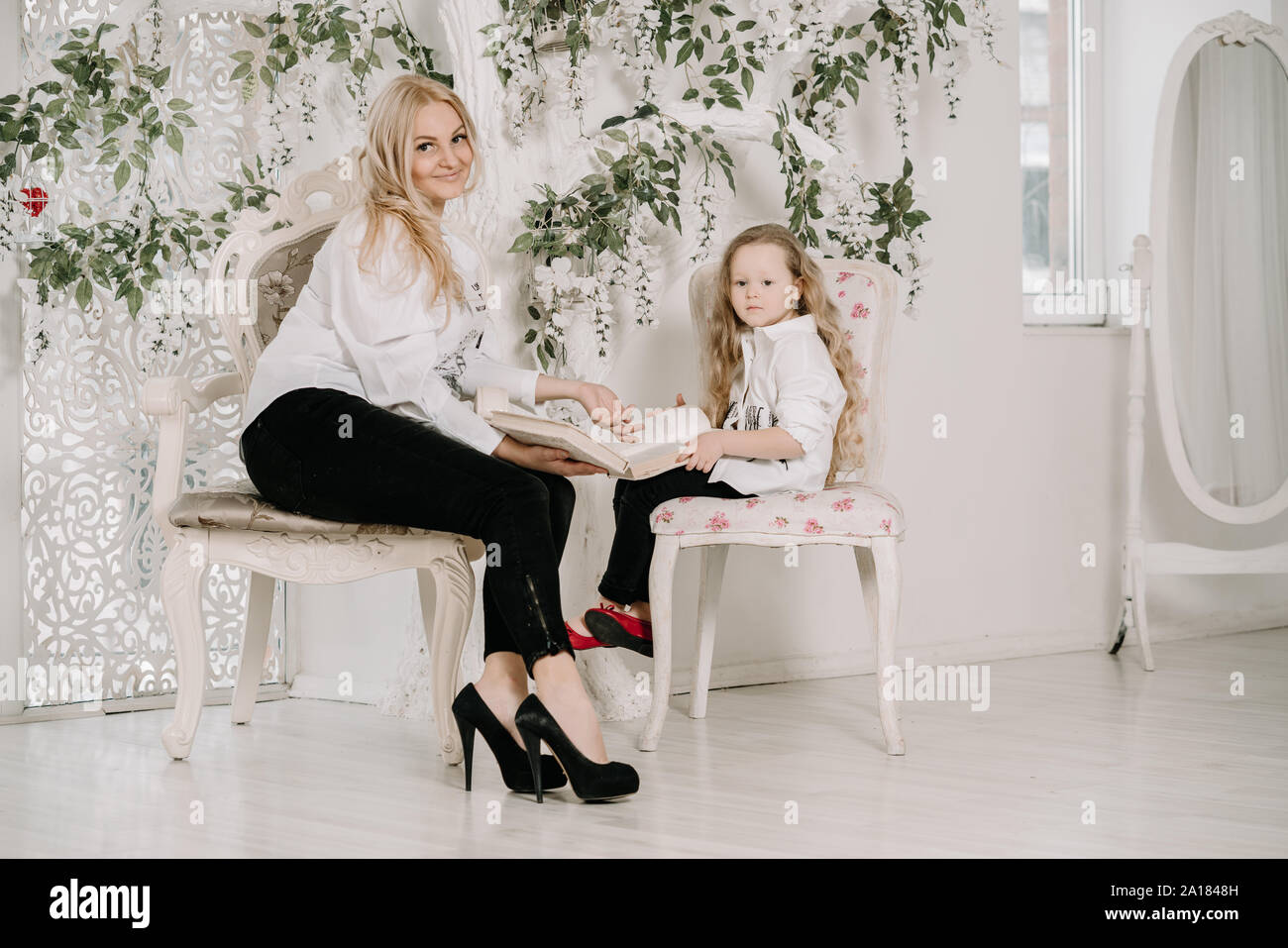 Ritratto di Madre e figlia in interni felice seduta vicino e la lettura di libri insieme in ambienti chiusi in camera bianca. Foto Stock