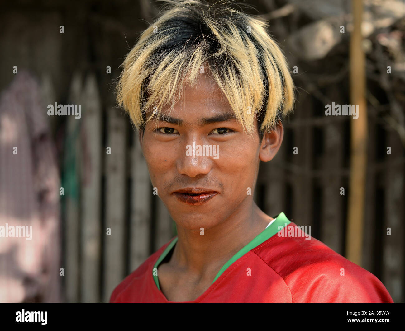 Giovane uomo birmano con biondo-capelli tinti e rosso, betel-colorate labbra mastica un betel quid (betel leaf, noci di arec dado, calce idrata, spezie e tabacco). Foto Stock