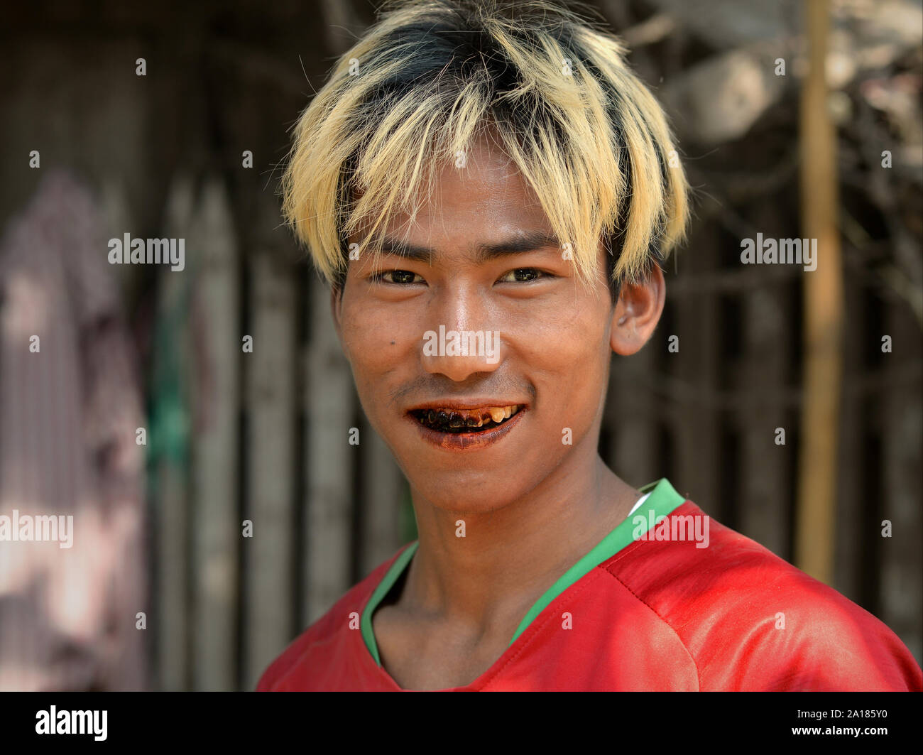 Giovane uomo birmano con biondo-capelli tinti e nero, betel-macchiato e denti cariati mastica un betel quid. Foto Stock