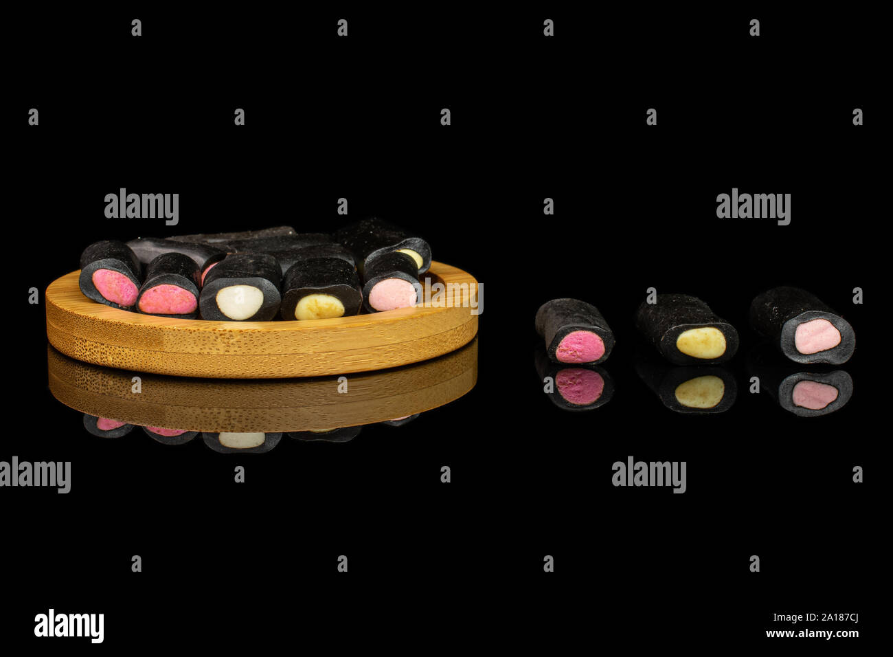 Sacco di tutto il dolce di liquirizia nera caramella sul bambù coaster isolato sul vetro nero Foto Stock