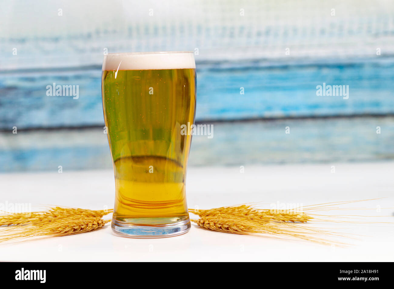 La pinta di birra con le spighe secche fiori di grano su un tavolo bianco con un colorato in legno texture a parete Foto Stock