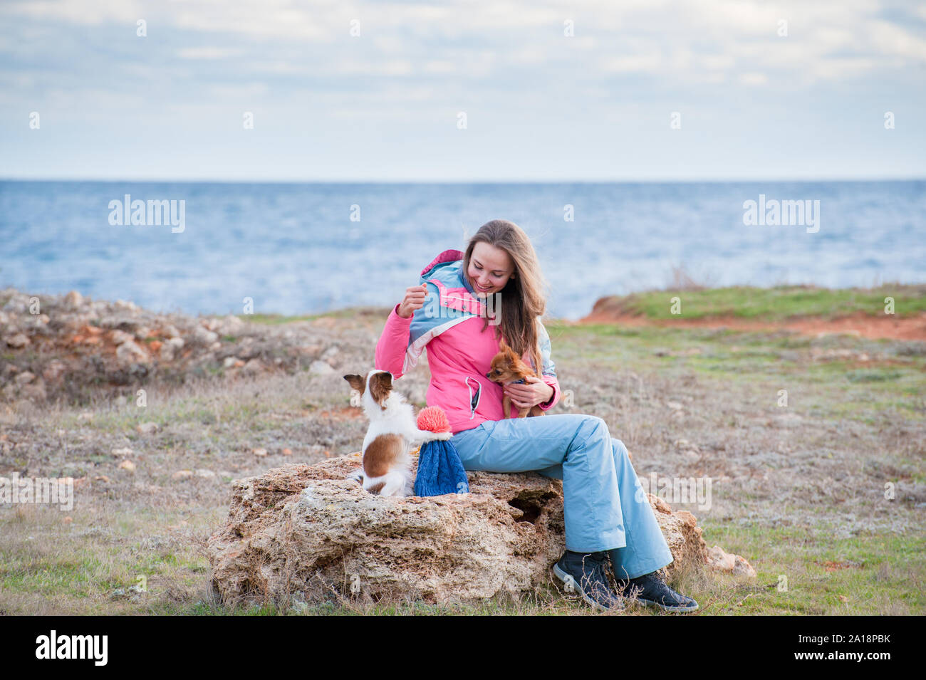 Felice bella femmina in tuta la sua formazione poco simpatici cani chihuahua fare trucchi vicino al mare in primavera Foto Stock
