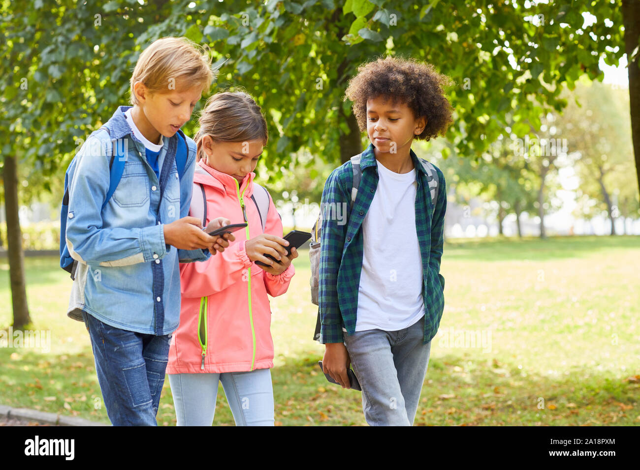 Un gruppo di bambini della scuola in abbigliamento casual camminare insieme nel parco e utilizzando i telefoni cellulari Foto Stock