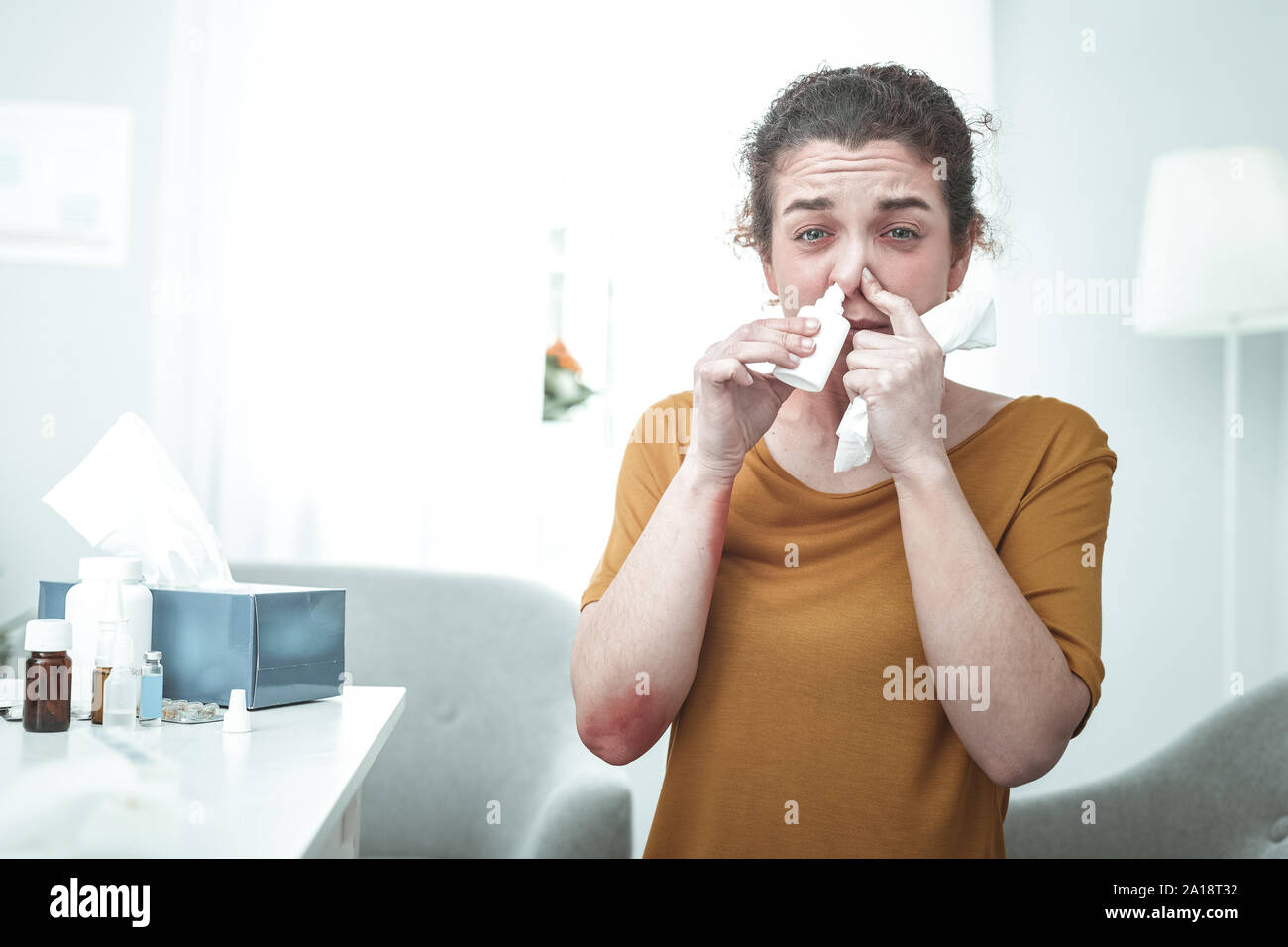 Curly donna che indossa maglietta arancione mediante spray nasale avente allergia Foto Stock