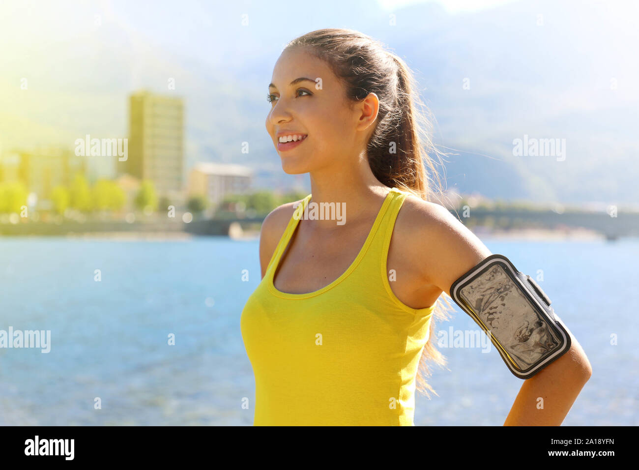 Donna fitness con fascia da braccio per la tecnologia telefonica facendo maratona in esecuzione esercizio jogging stretching caldo al mattino in città sul lago. Foto Stock