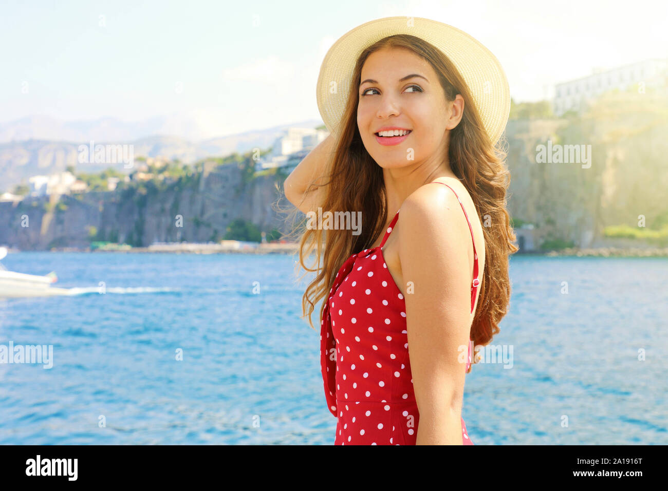 Moda ragazza godendo di vista nella città di Sorrento, Italia. Bellissimo modello con abito rosso e cappello con la Penisola Sorrentina sullo sfondo. Foto Stock
