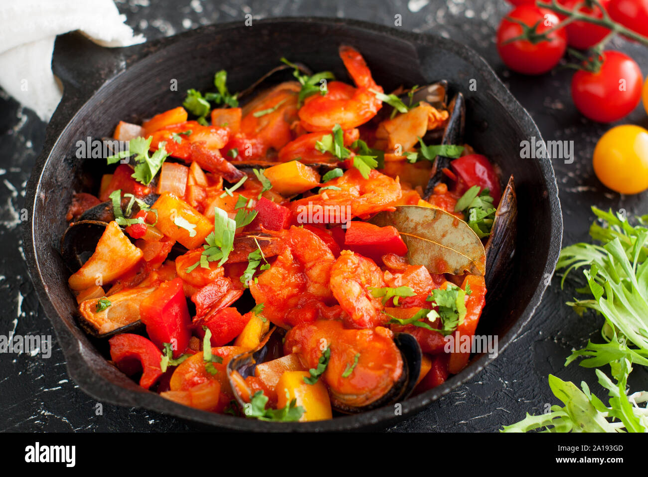 Stufato di pesce cioppino con gamberetti, capesante, vongole, cozze e pesce in padella sulla tavola nera, servita con verdure Foto Stock