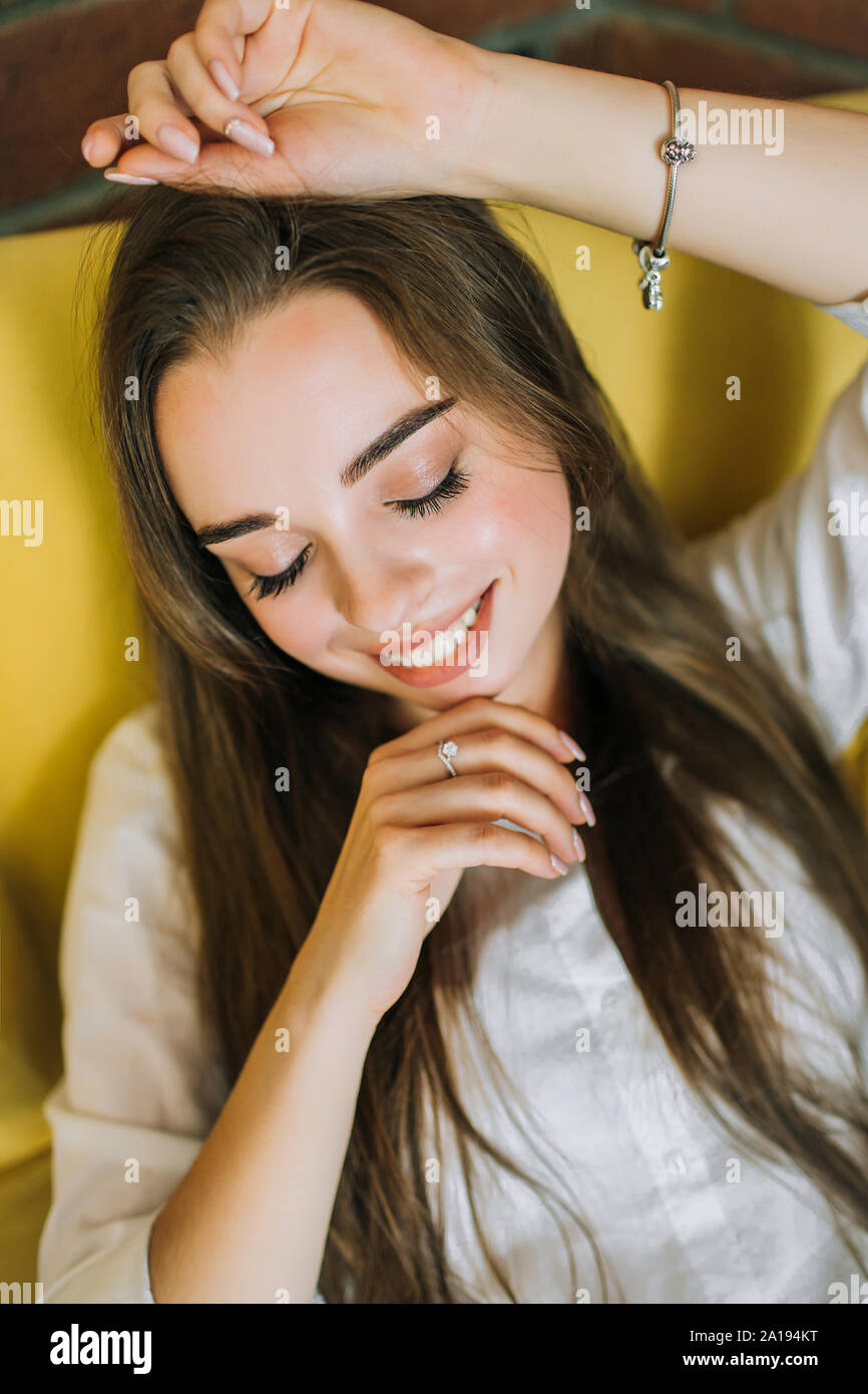 Ritratto di una giovane donna bellissima con scuri capelli lunghi, seduto in una sedia di colore giallo con i suoi occhi teneramente chiuso, sorridente. Foto Stock