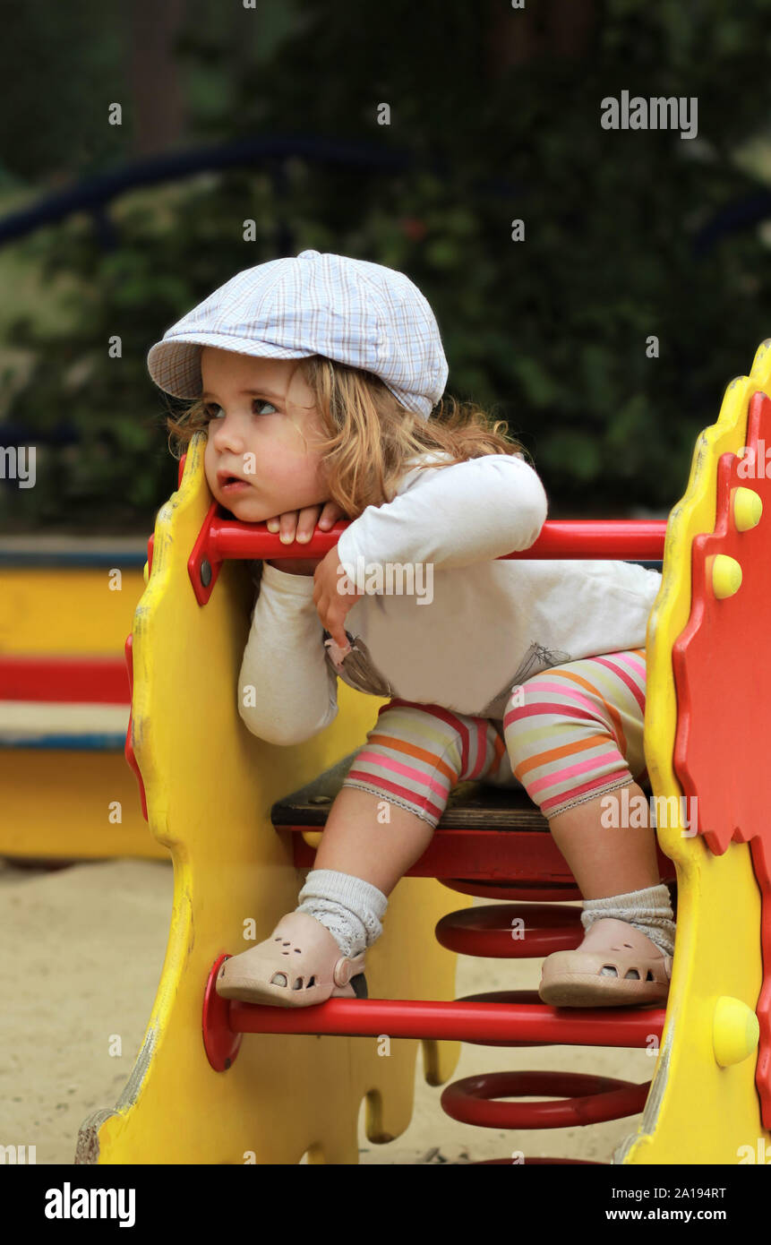 Considerato elegante un anno vecchio ragazza in un cappuccio controllati seduto su un parco giochi Foto Stock