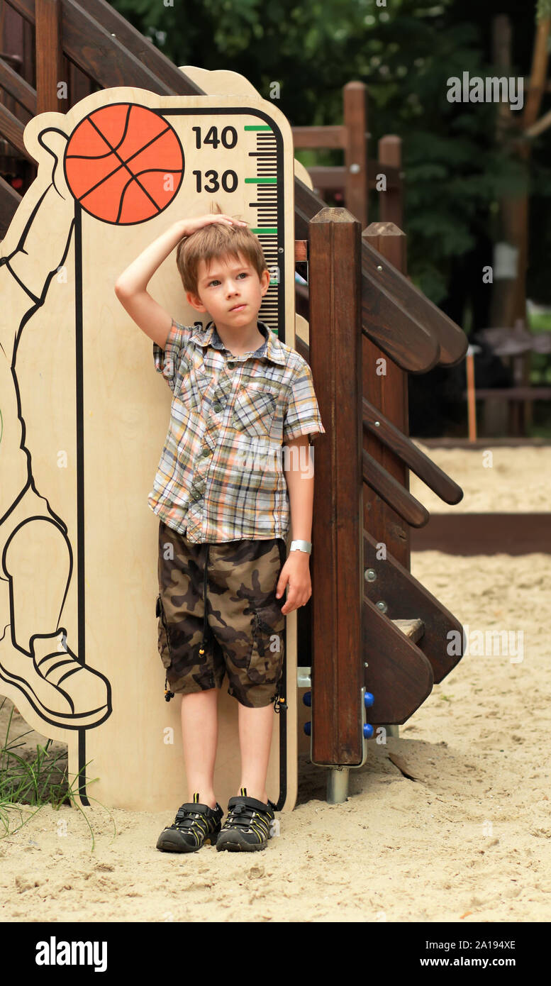 Cinque anni di vecchio ragazzo misurando la sua altezza sul parco giochi per bambini Foto Stock