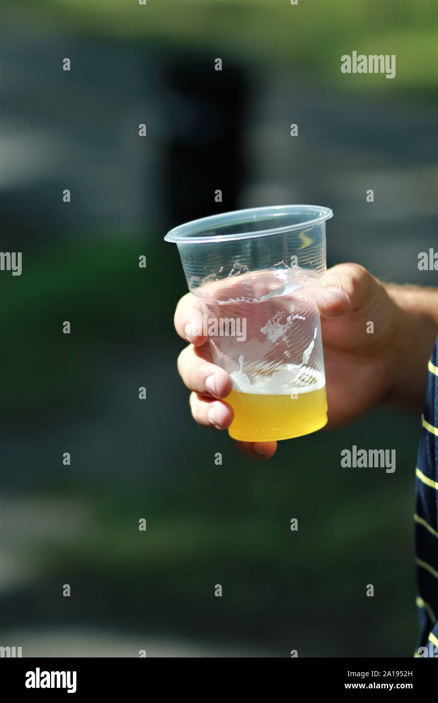 Close up di un bicchiere di plastica della birra chiara attesa da mano maschio Foto Stock
