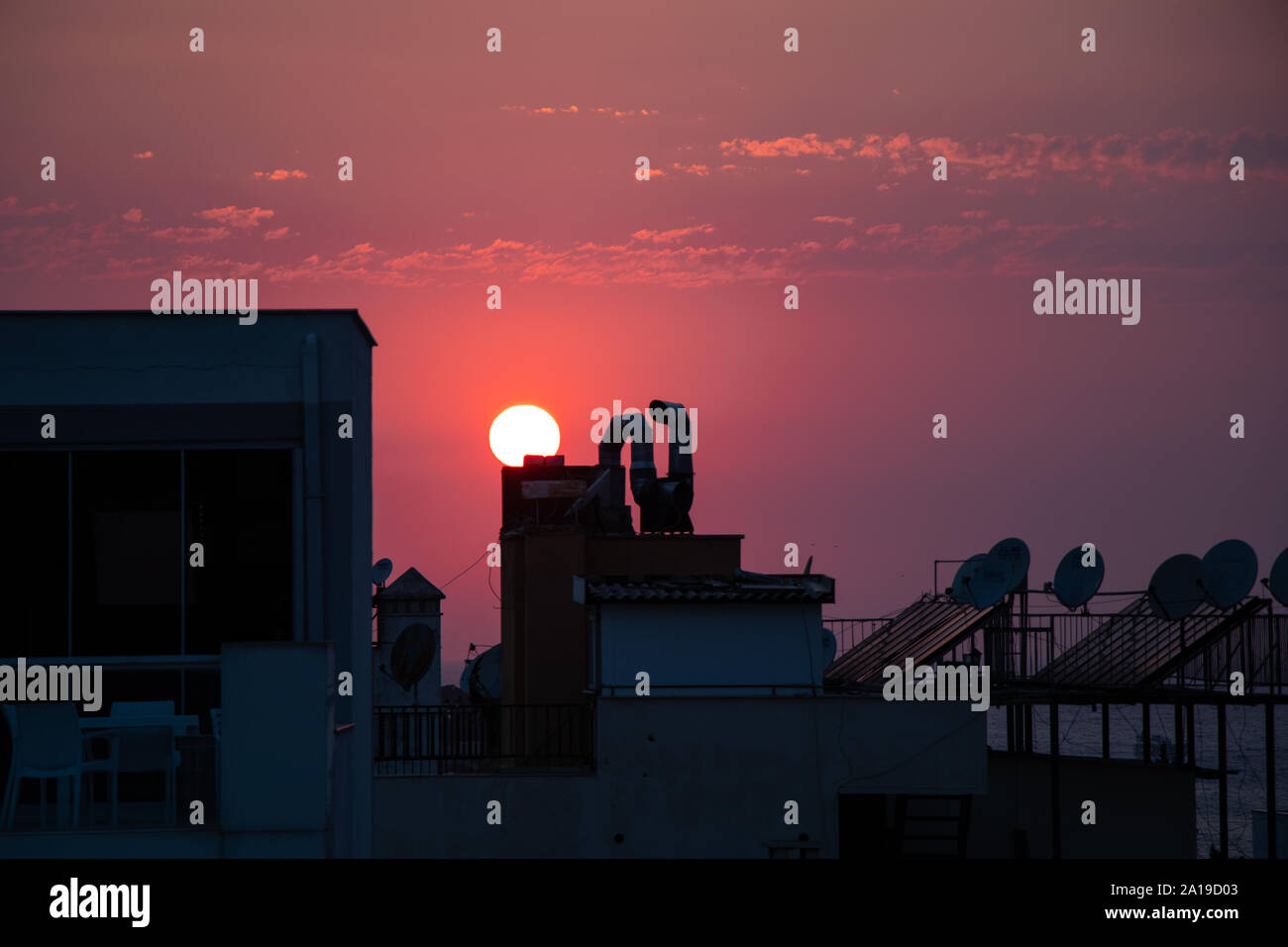 Il sole che tramonta dietro i tetti degli edifici rendendo il cielo viola. Foto Stock