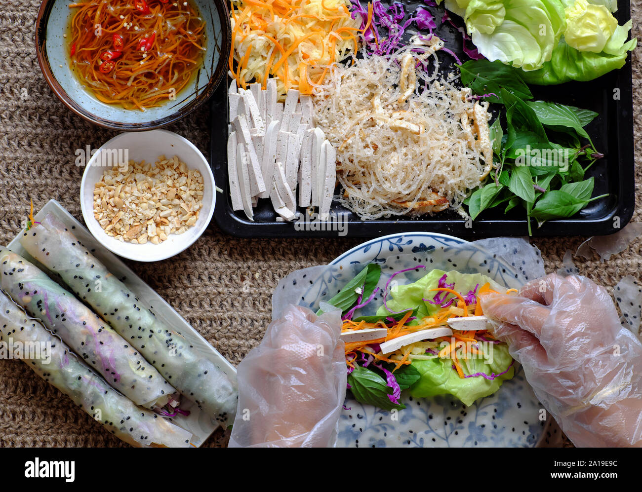 Vista dall'alto di persone però rendere vegane carta in rotoli di riso, vietnamita involtini primavera da lasciare come ingrediente di carota e di cavolo viola, salsiccia, vermicelli, tofu Foto Stock