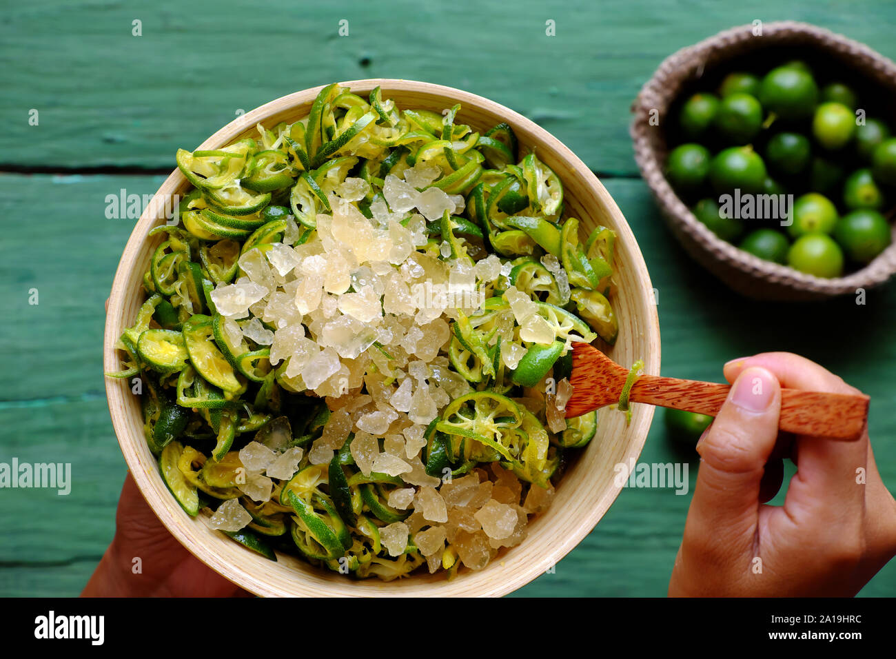 Vista dall'alto di persone tenere in mano una ciotola di kumquat peel fetta tagliata e mescolare con lo zucchero di roccia, questo aspro frutto ricco di vitamina C, sano e rendere detox drink Foto Stock