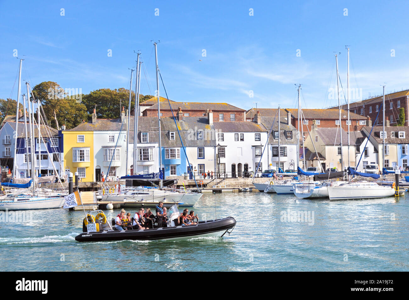 I turisti in una nervatura gita in barca nel porto vecchio passando il yacht e case a schiera su Noil Parade, Weymouth, Jurassic Coast, Dorset, England, Regno Unito Foto Stock