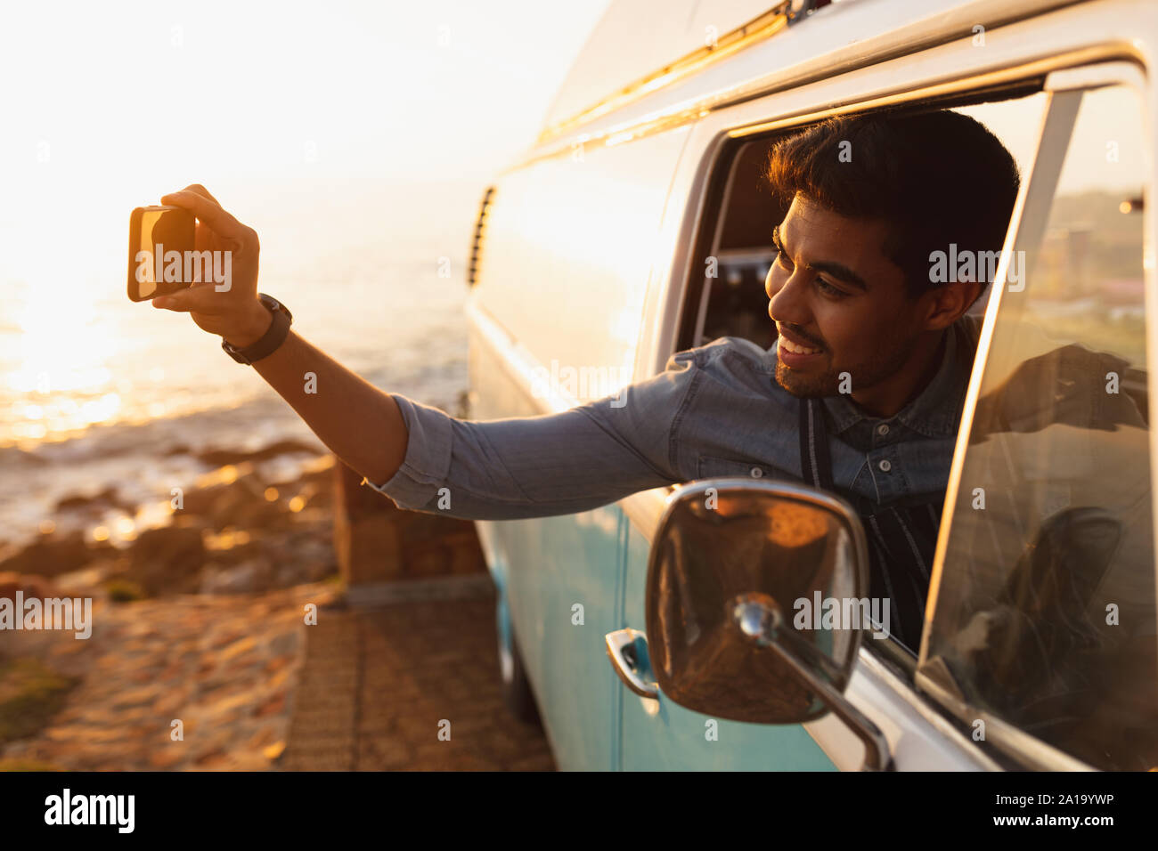 Giovani razza mista uomo seduto sul sedile anteriore di un furgone tenendo selfie Foto Stock