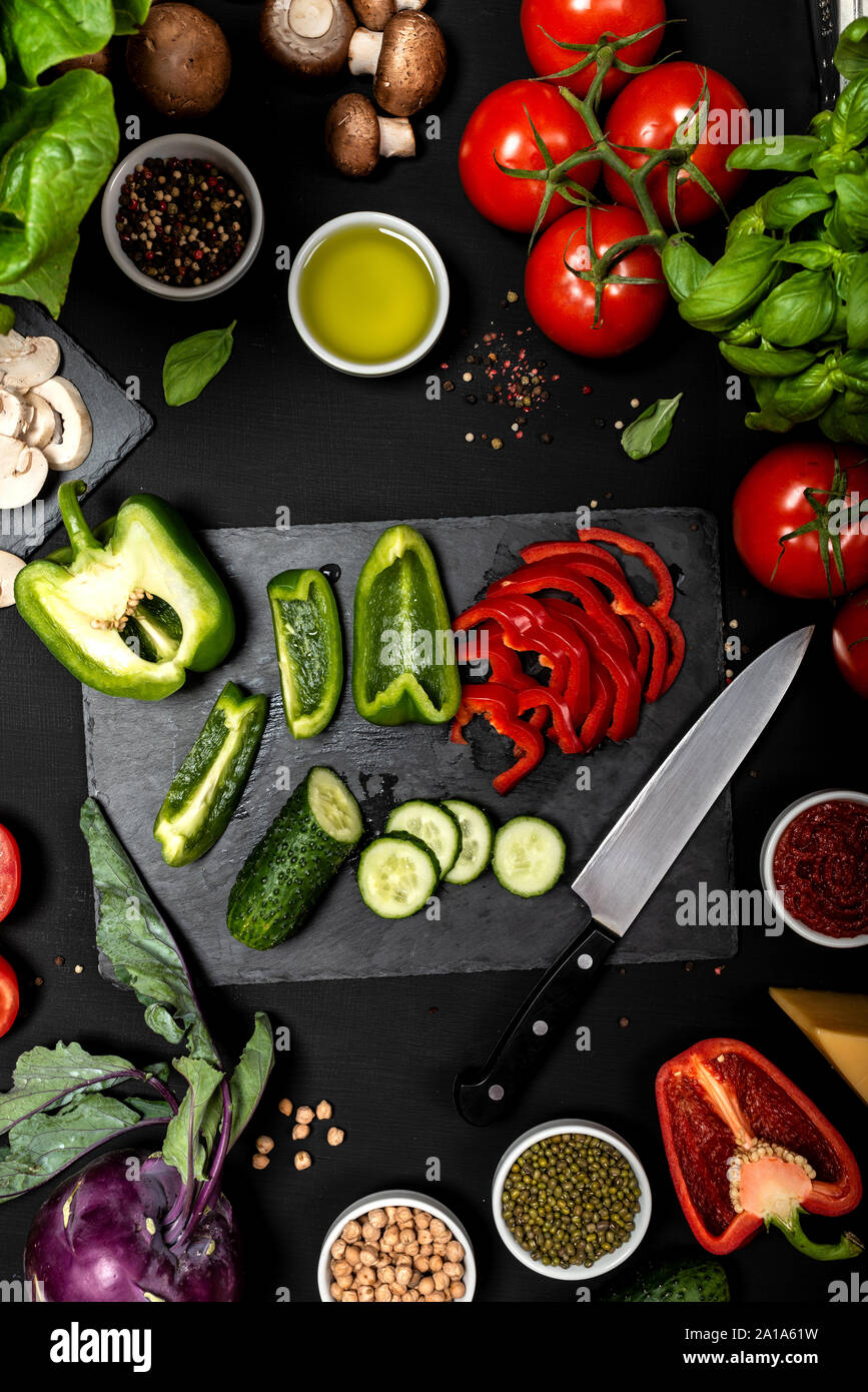 Ingredienti crudi per cucinare cibi sani vegetariani. Piatto di verdure e formaggi su fondo nero. Foto Stock