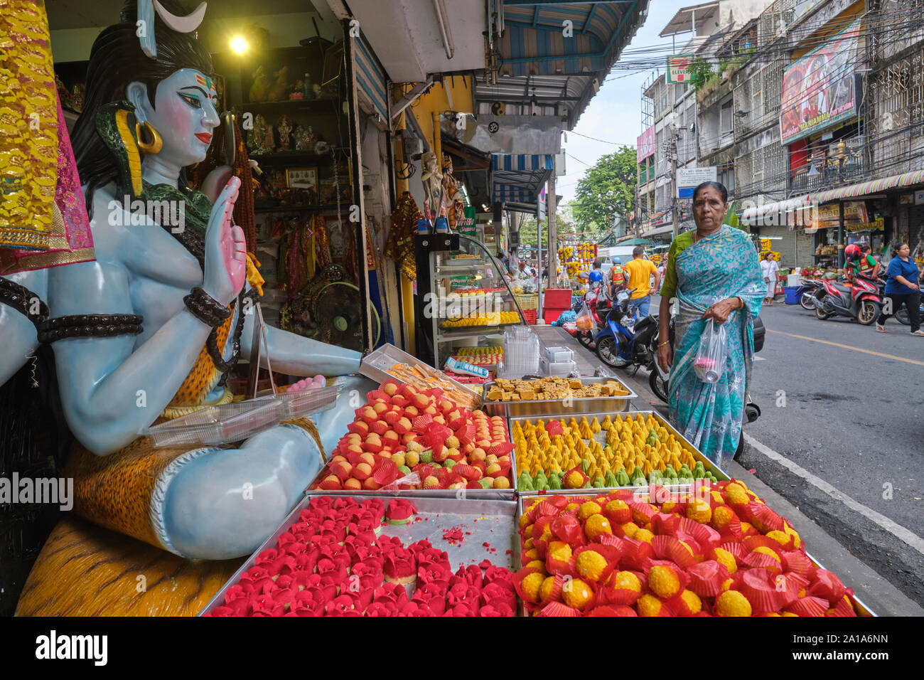 I dolci indiani stabiliti nella parte anteriore di un negozio indiano custodito da una statua di Shiva; accanto a Sri Mahamariammam (Hindu) Tempio in Silom Rd., Bangkok, Thailandia Foto Stock