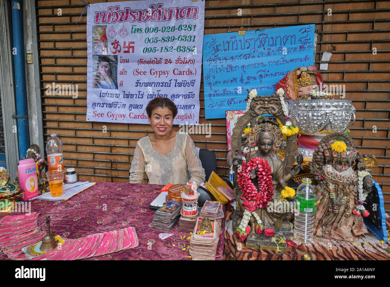 Una femmina di fortune teller con utensili del suo mestiere e statue di divinità Indù, seduto di fronte a un tempio indù in Silom Rd., Bangkok, Thailandia Foto Stock Una femmina di fortune teller con utensili del suo mestiere e statue di divinità Indù, seduto di fronte a un tempio indù in Silom Rd., Bangkok, Thailandia Foto Stock