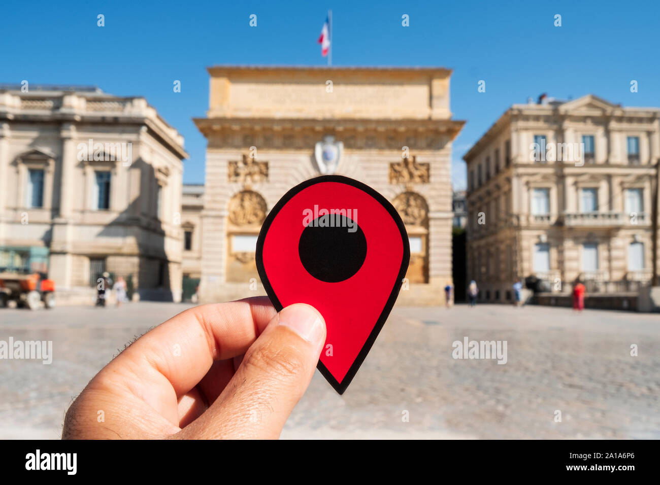 Primo piano della mano di un uomo caucasico tenendo un contrassegno rosso presso la Porte du Peyrou cancello in Montpellier, Francia Foto Stock