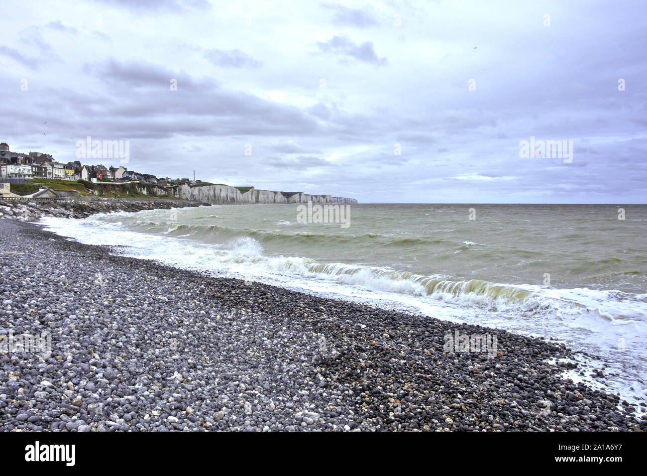 Plage d'onival par temps couvert et marée haute, vagues et écume sur la plage de galets, falaises en fond et ville d'Ault. Foto Stock