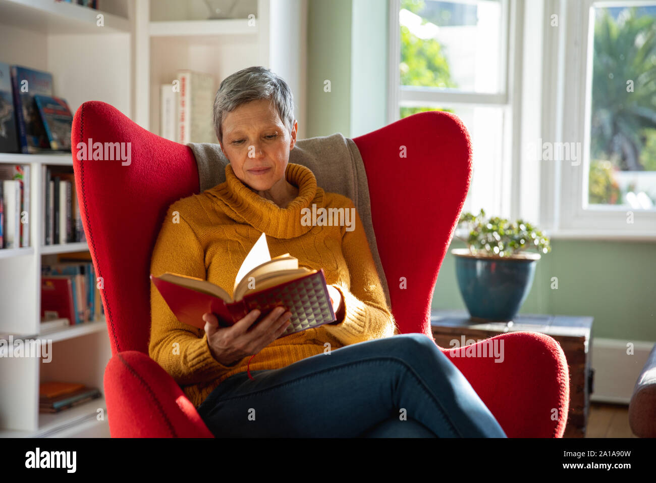 Donna matura a casa da sola lettura prenota Foto Stock
