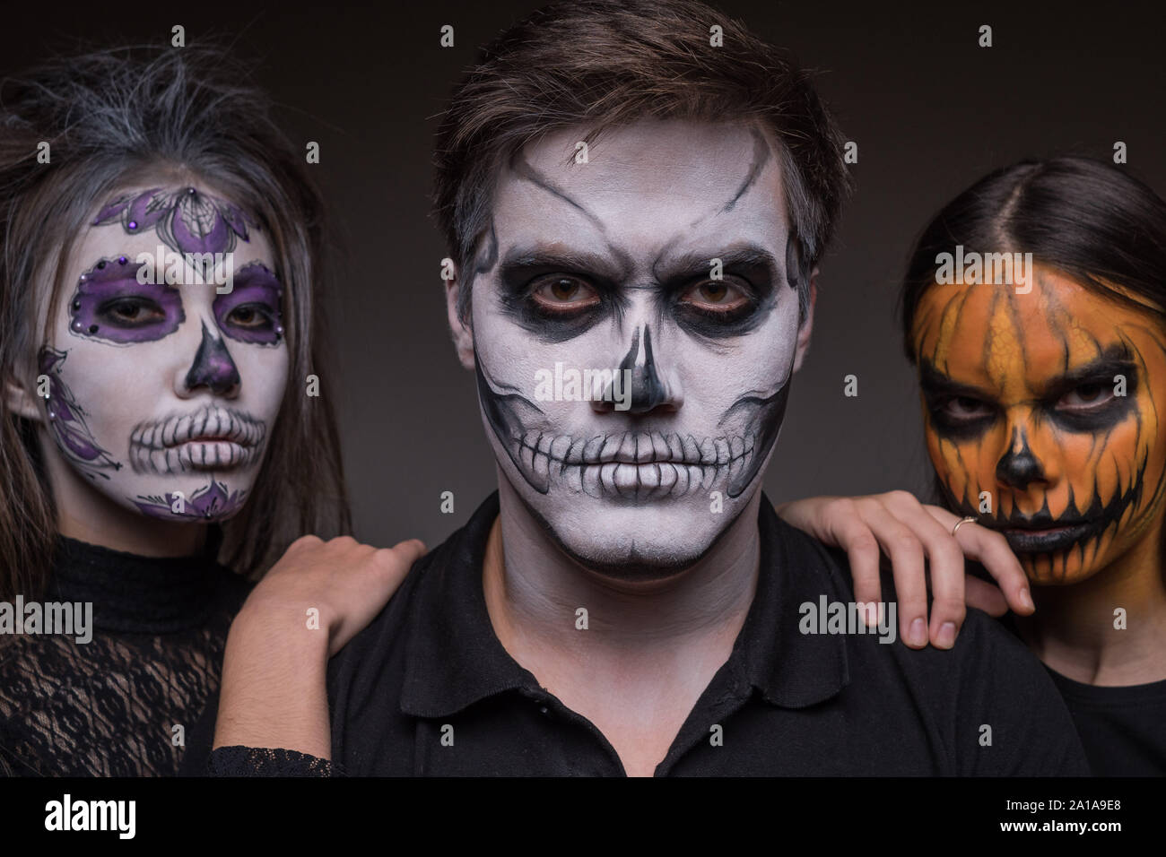 Close-up di un ragazzo con una maschera del cranio e due ragazze come scheletri in background. Preparazione per la festa di Halloween. Foto Stock