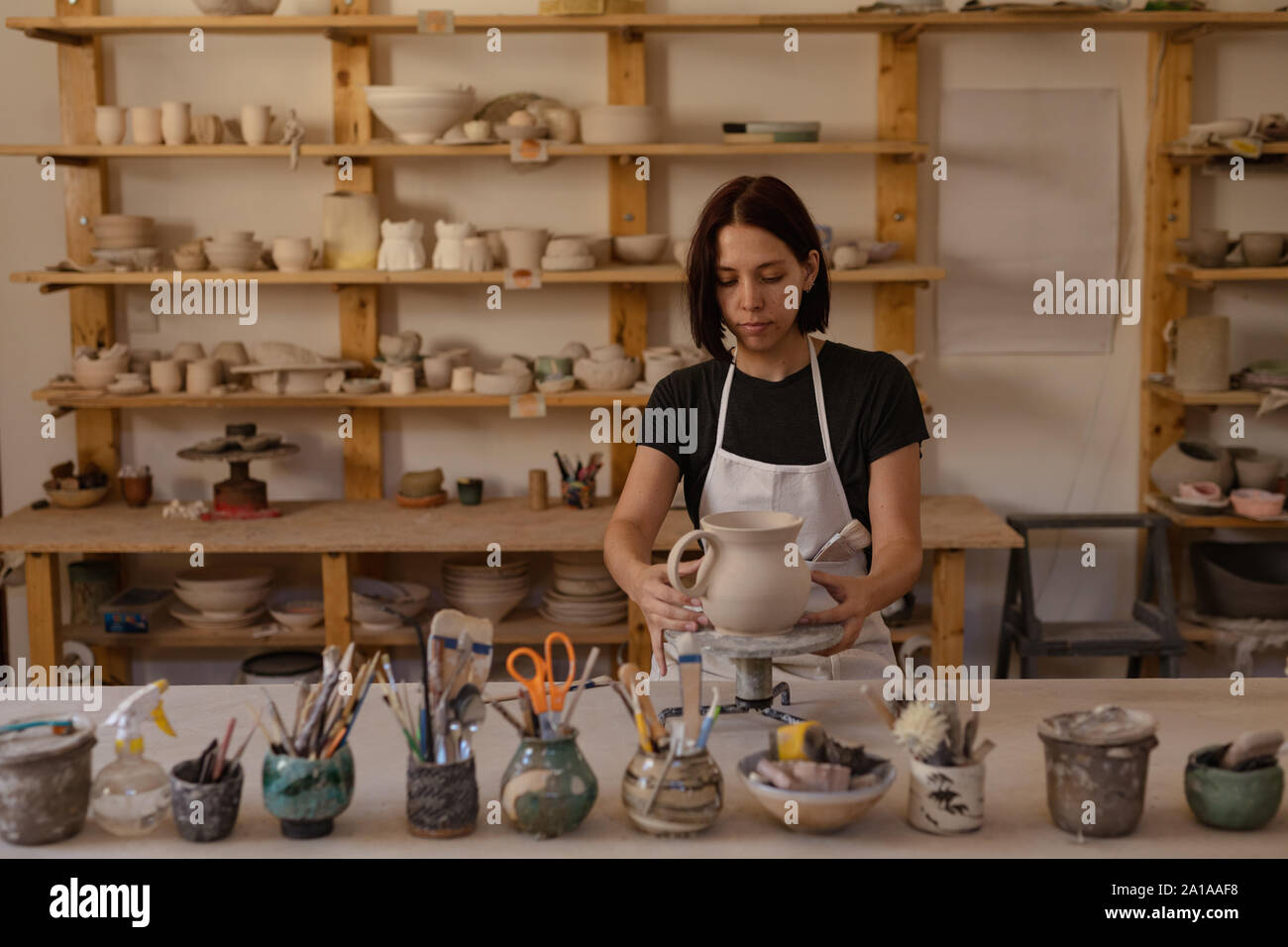 Potter femmina in un ceramiche studio tenendo una brocca su una ruota di fascettatura Foto Stock