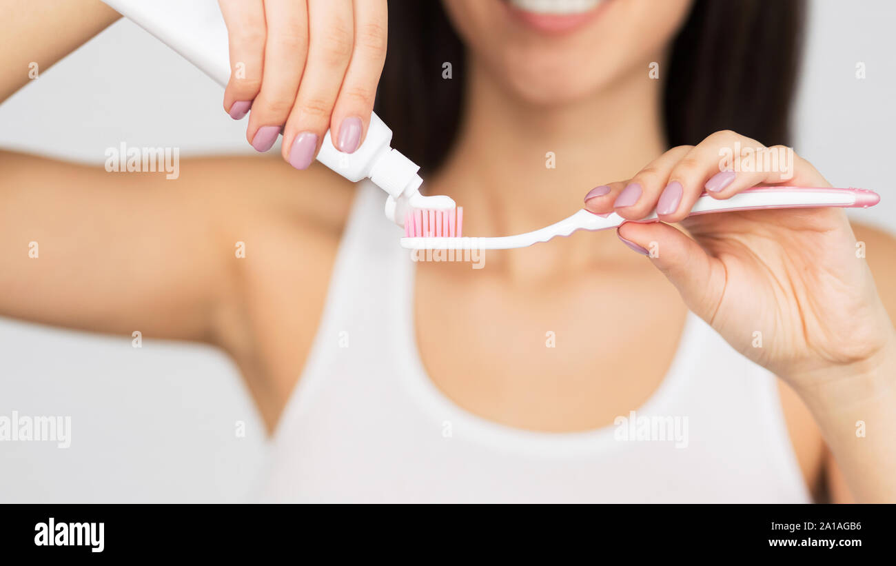 Irriconoscibile donna mettendo il dentifricio su uno spazzolino da denti, sfondo bianco, Panorama Foto Stock