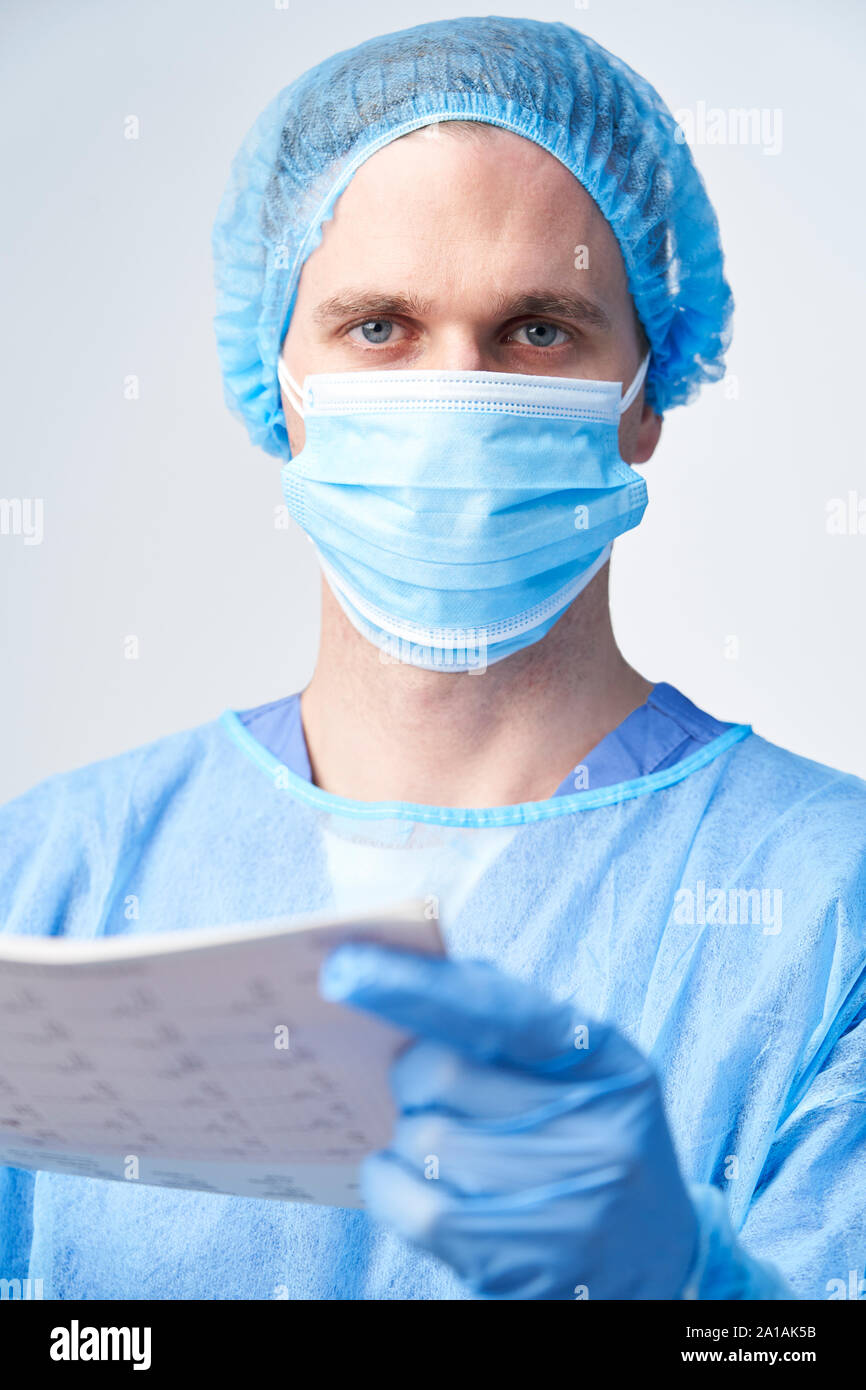 Ritratto in studio di chirurgo maschio indossando camice e maschera Holding Medical Stampare Foto Stock