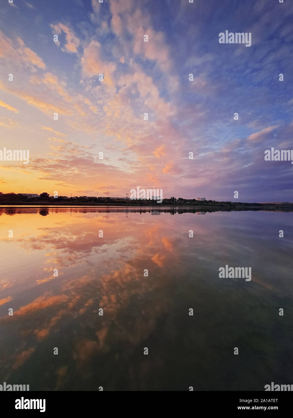 Colpo verticale soffici nuvole colorate che riflette il tramonto sul lago di superficie di acqua. Calma, idilliaco scena serale con un sacco di nuvole sopra il laghetto. Foto Stock