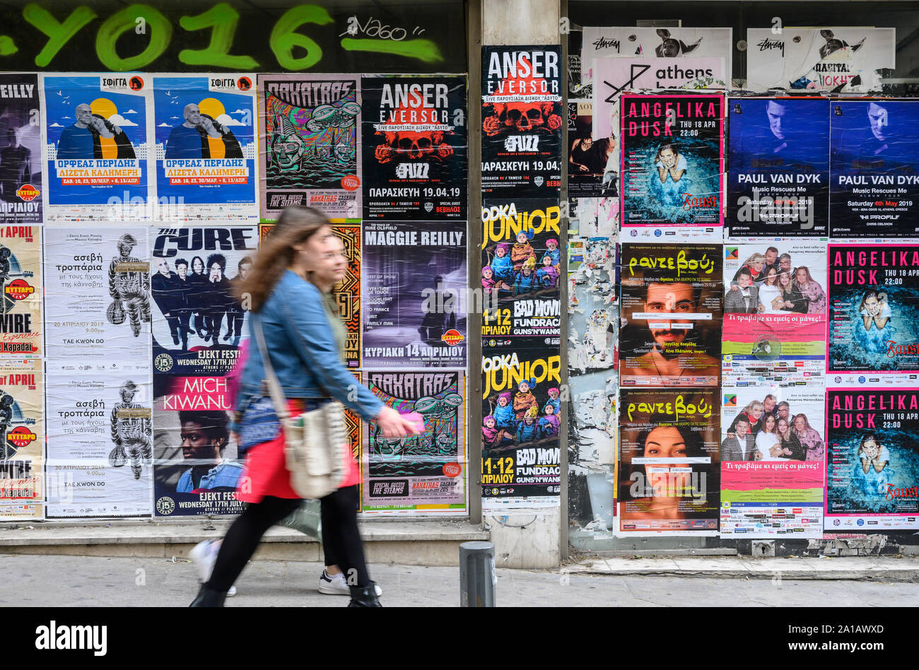 Due donne cammina davanti ad una parete del poster di intrattenimento nel centro di Atene, Grecia Foto Stock