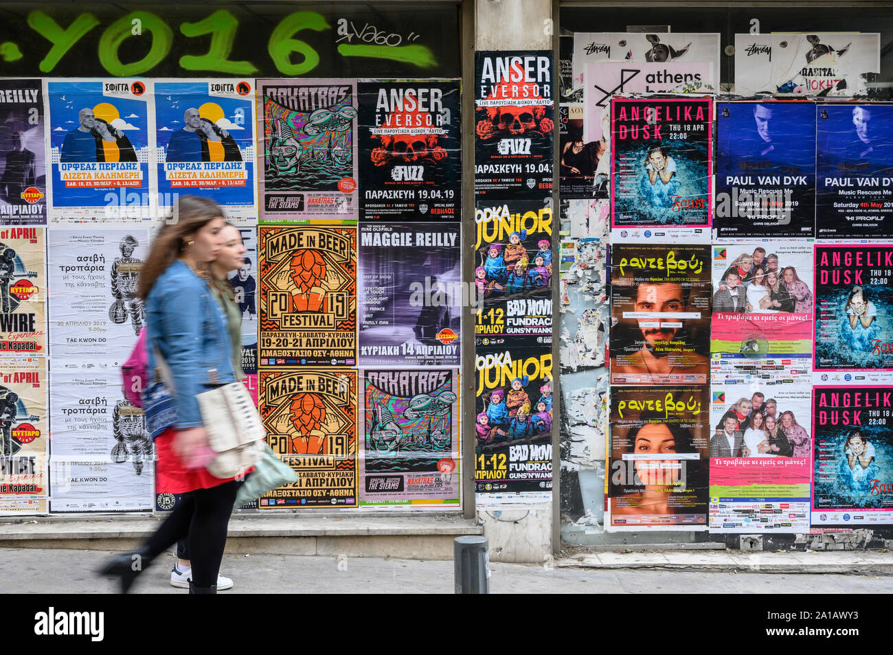 Due donne cammina davanti ad una parete del poster di intrattenimento nel centro di Atene, Grecia Foto Stock