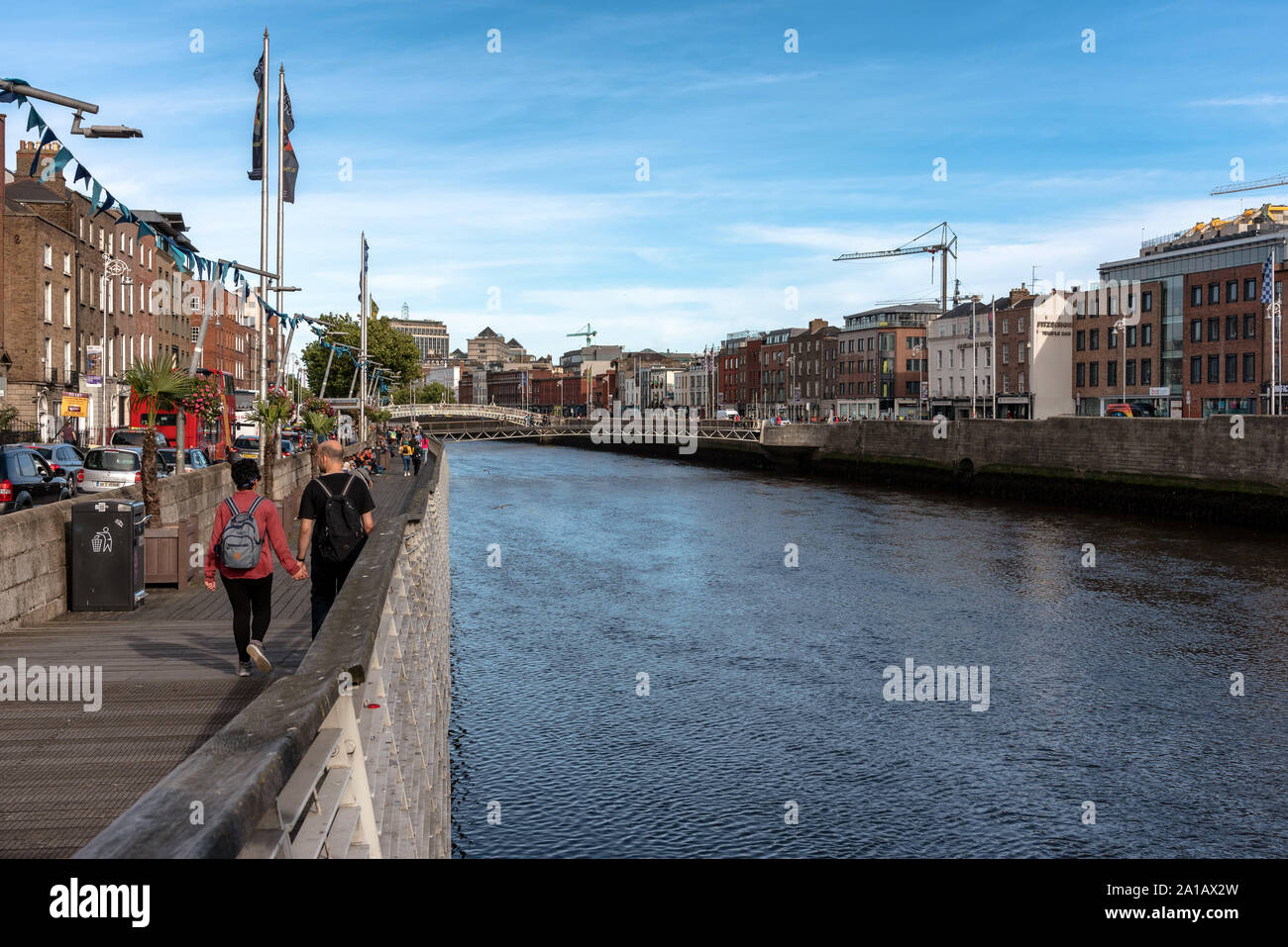 La gente che camminava sul fiume Liffey Boardwalk con il Millennio e Ha'penny ponti in background in Dublino, Irlanda Foto Stock