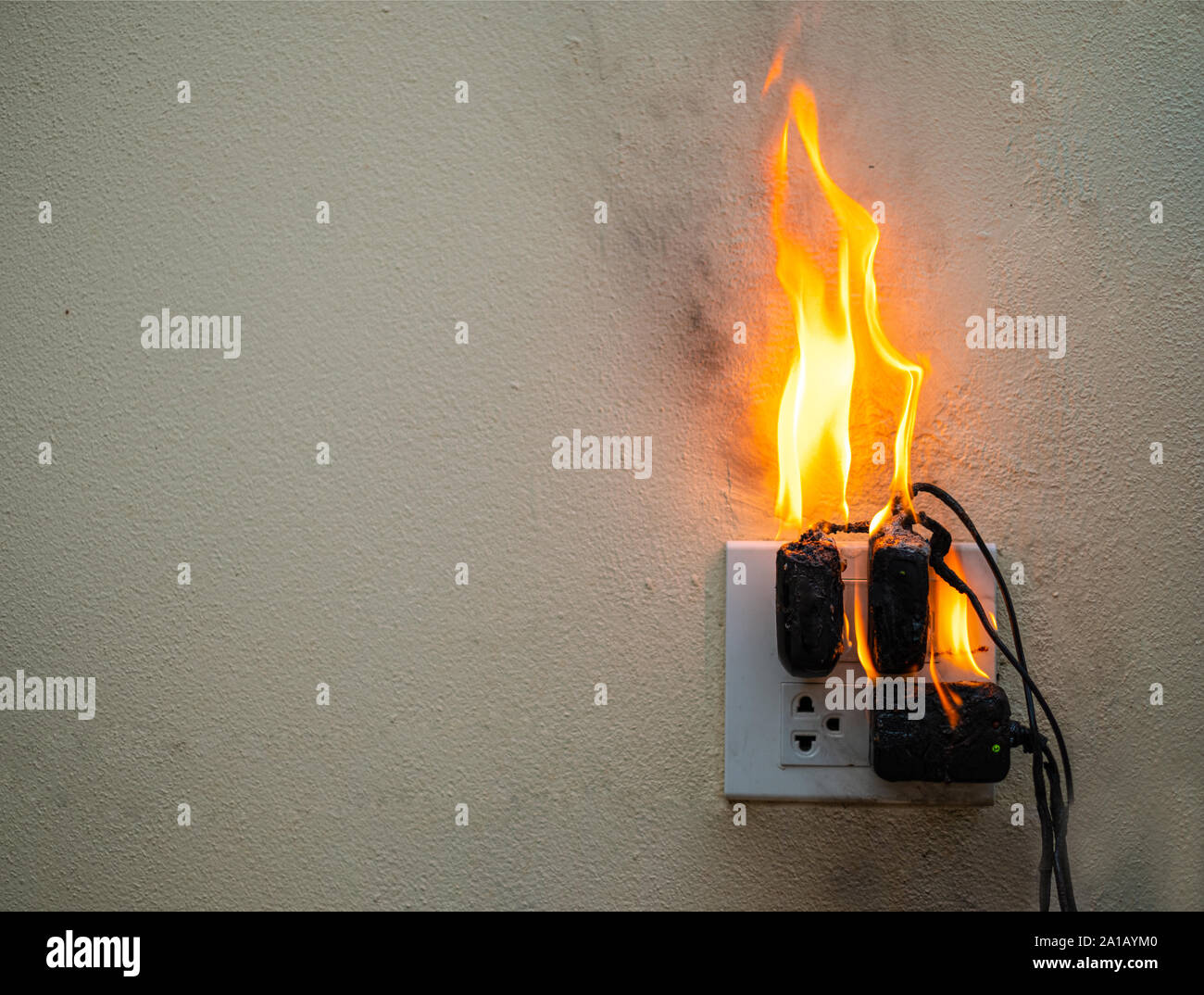 Sul fuoco un adattatore a spina femmina su sfondo bianco, corto circuito elettrico a guasto derivante in elettricità filo bruciato Foto Stock