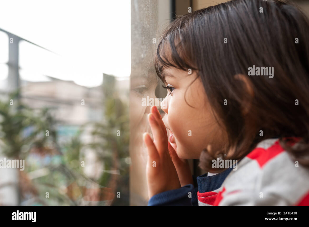 Carino littell ragazza di guardare attraverso una finestra a casa Foto Stock