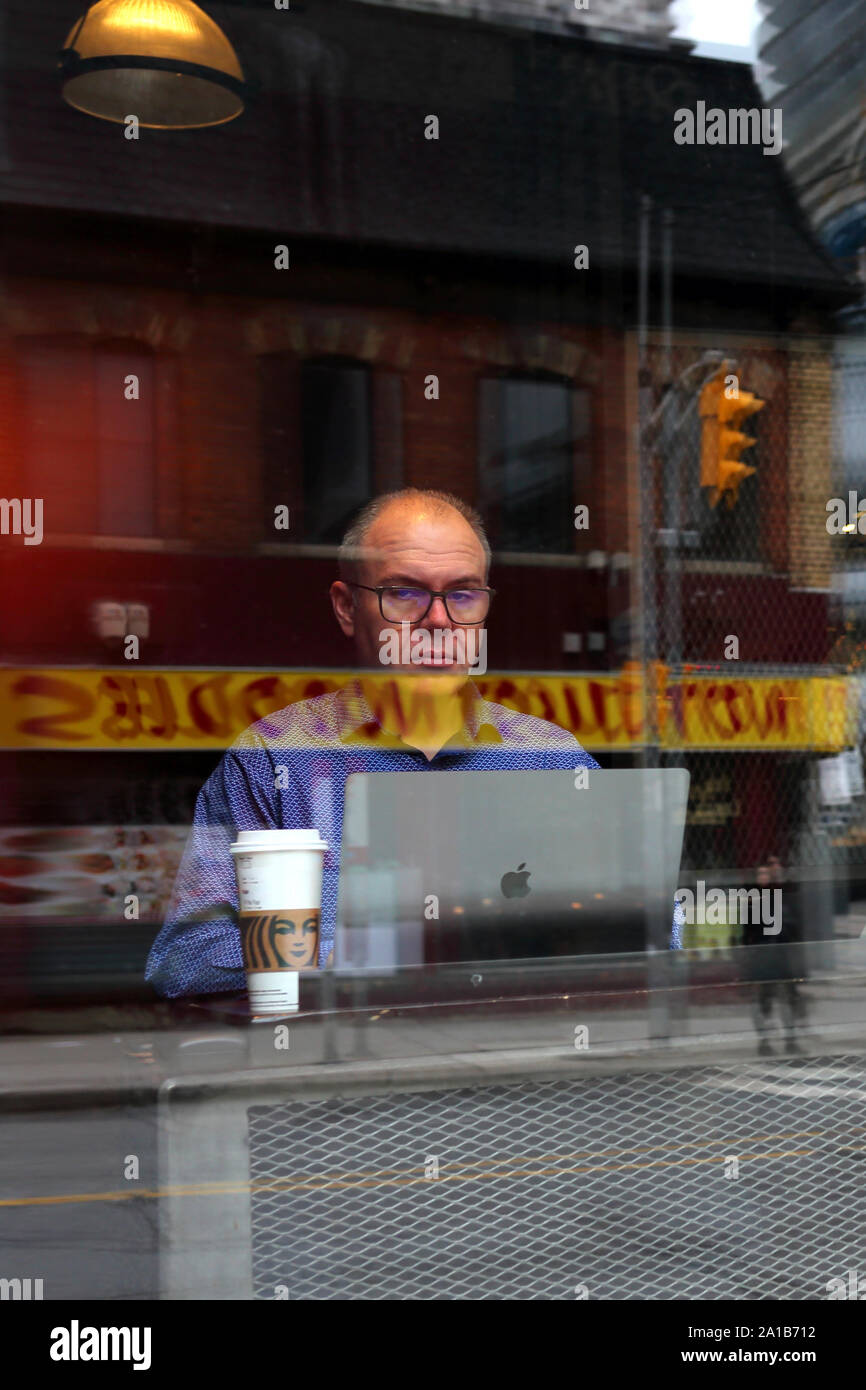 Uomo seduto dietro il suo macbook Apple presso Starbucks. Una tazza di Starbucks si siede sul tavolo accanto a lui. Foto Stock