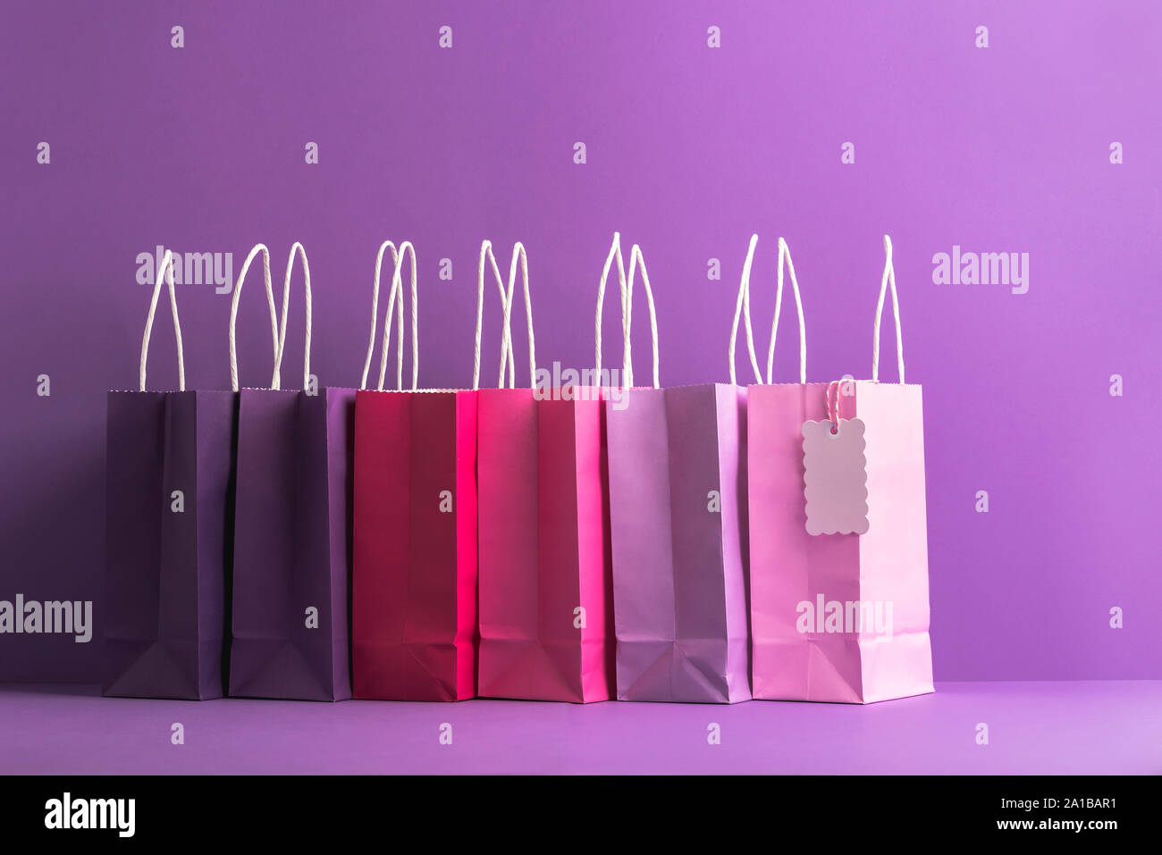 Shopping di Natale concetto con varie sfumature di viola la carta shopping bags su uno sfondo viola. Sacchetti di carta con manici e tag vuoto. Foto Stock