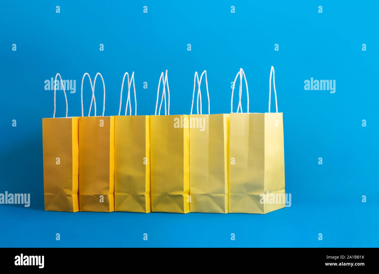 Carta shopping bags in una fila, in sfumature di giallo, in stile minimalista sfondo blu. Shopping di Natale tema. Concetto di regali. Colorato presenta borse Foto Stock