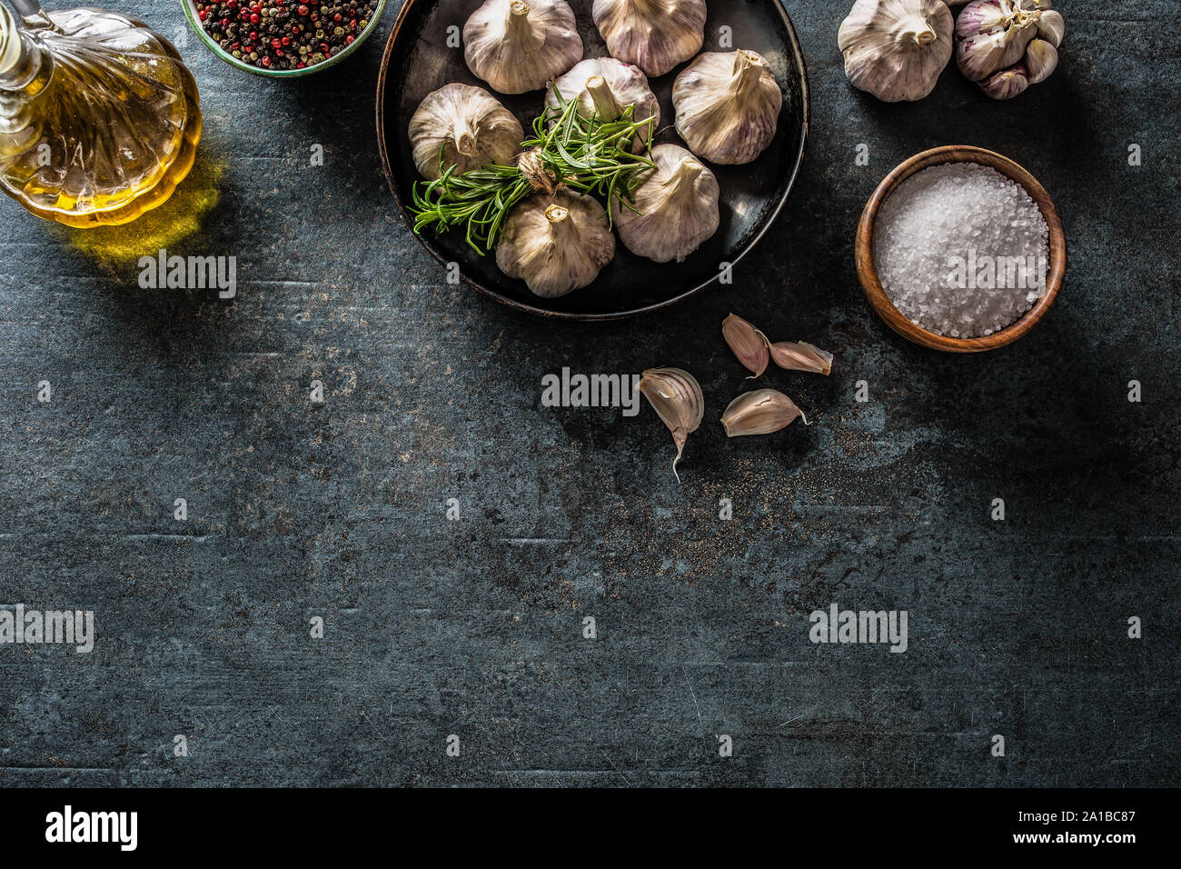 4 spicchi di aglio e la lampadina in padella con rosmarino fresco olio di oliva sale e spezie su cemento tabella Foto Stock