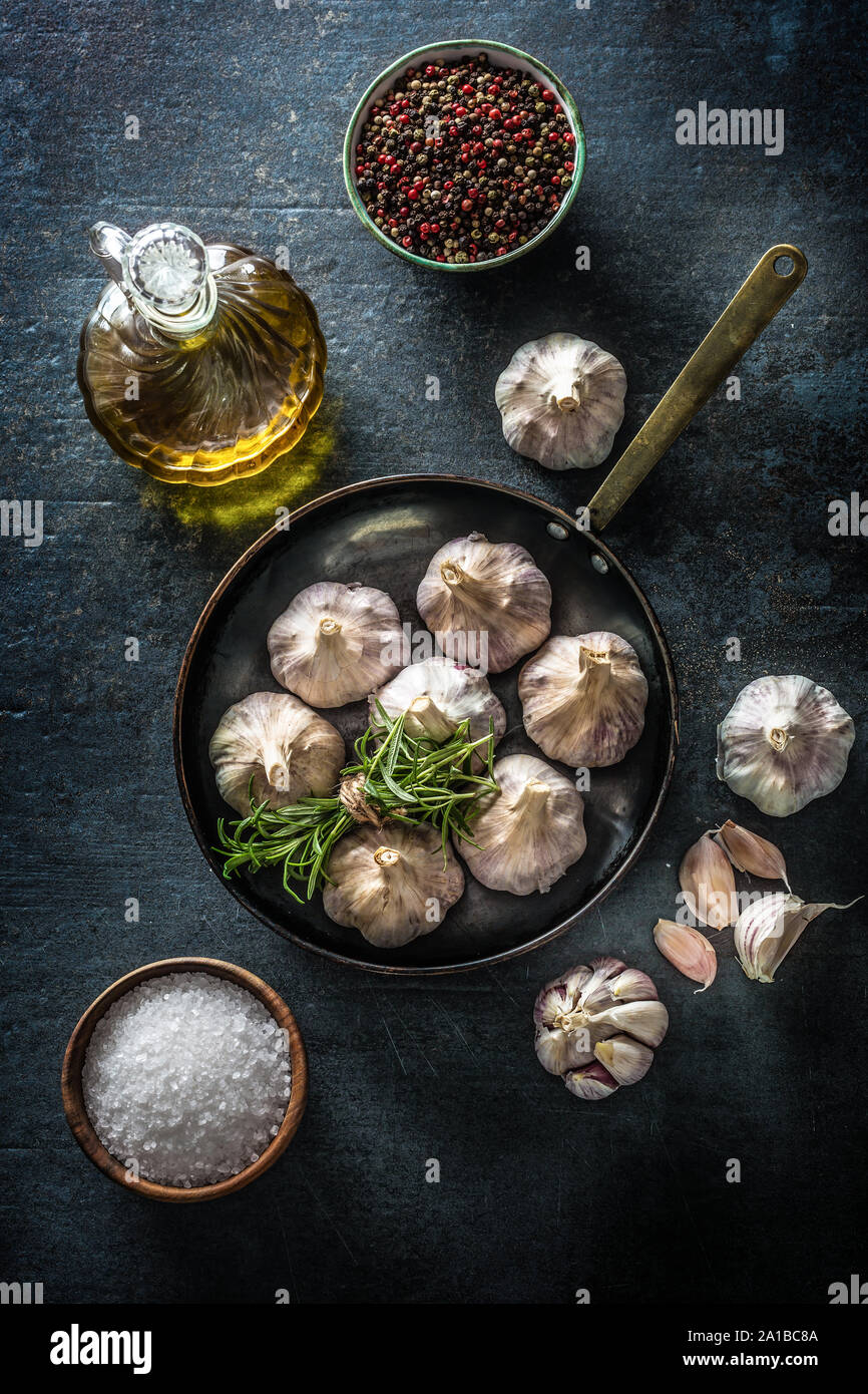 4 spicchi di aglio e la lampadina in padella con rosmarino fresco olio di oliva sale e spezie su cemento tabella Foto Stock