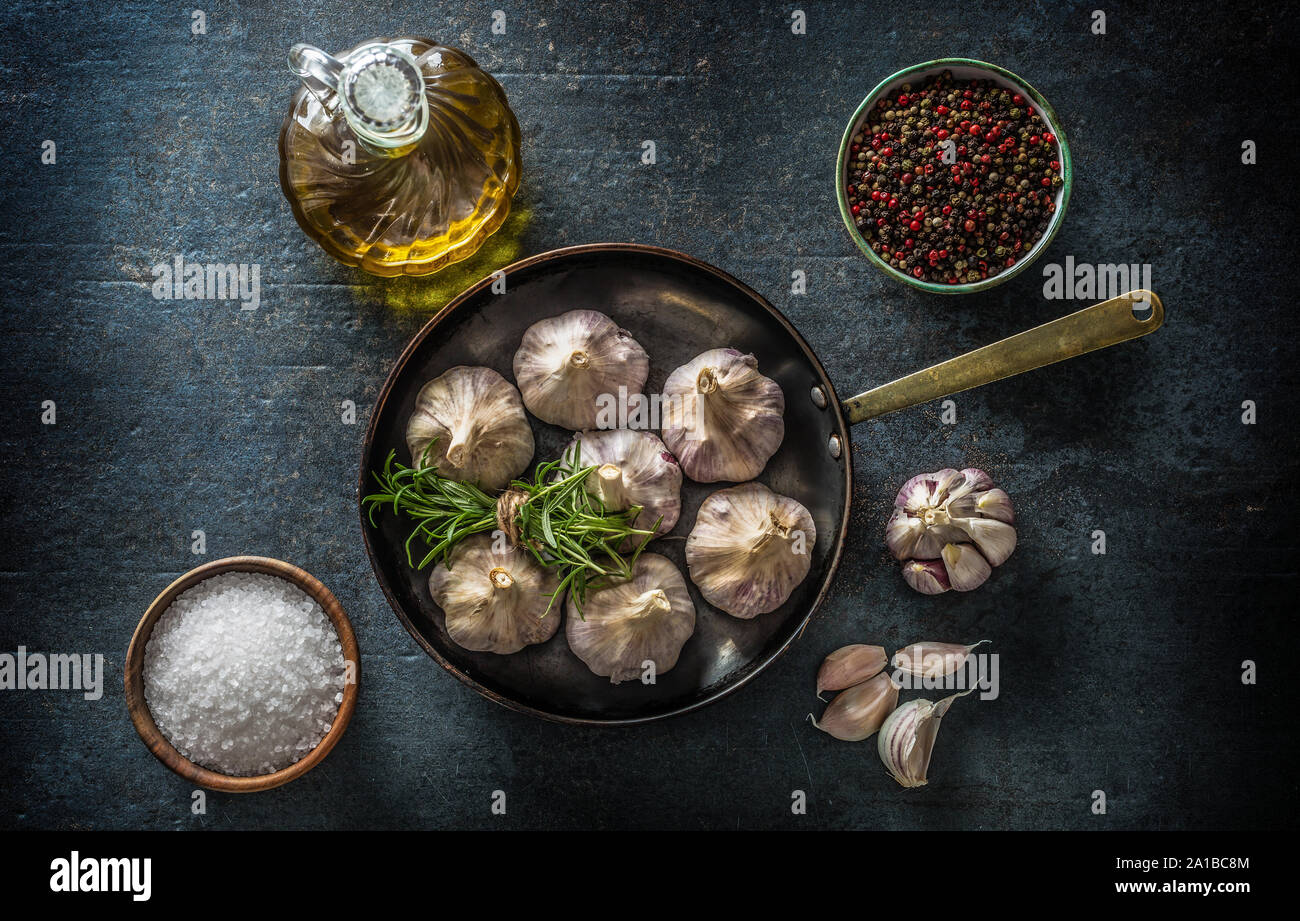 4 spicchi di aglio e la lampadina in padella con rosmarino fresco olio di oliva sale e spezie su cemento tabella Foto Stock