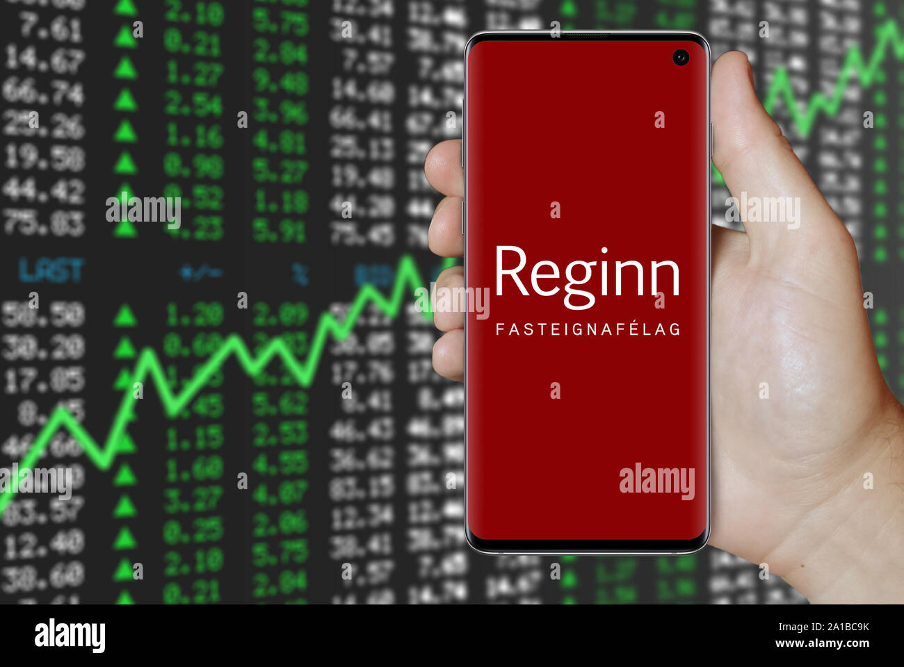 Un uomo possiede uno smartphone visualizzando il logo della società Reginn quotata al Nasdaq Islanda. Positivo del mercato azionario sfondo. Credito: PIXDUCE Foto Stock