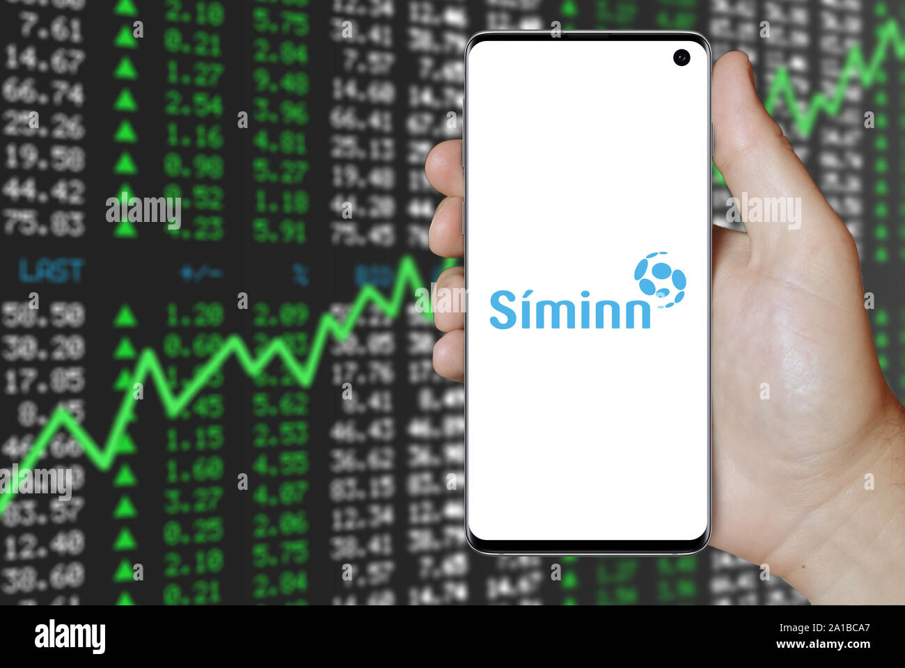 Un uomo possiede uno smartphone visualizzando il logo della società Síminn quotata al Nasdaq Islanda. Positivo del mercato azionario sfondo. Credito: PIXDUCE Foto Stock