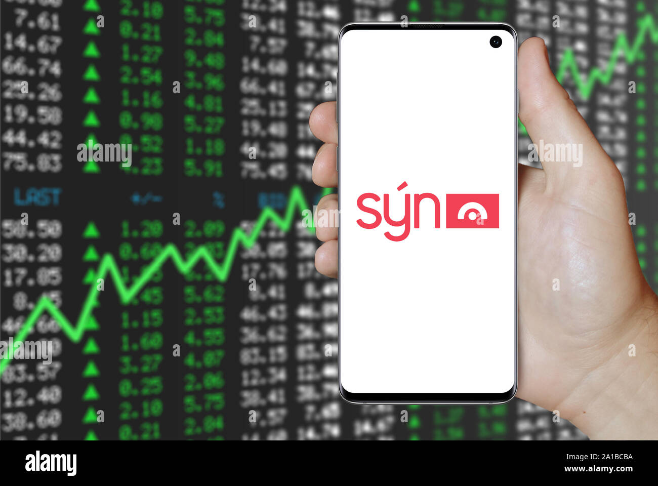 Un uomo possiede uno smartphone visualizzando il logo della società Sýn quotata al Nasdaq Islanda. Positivo del mercato azionario sfondo. Credito: PIXDUCE Foto Stock