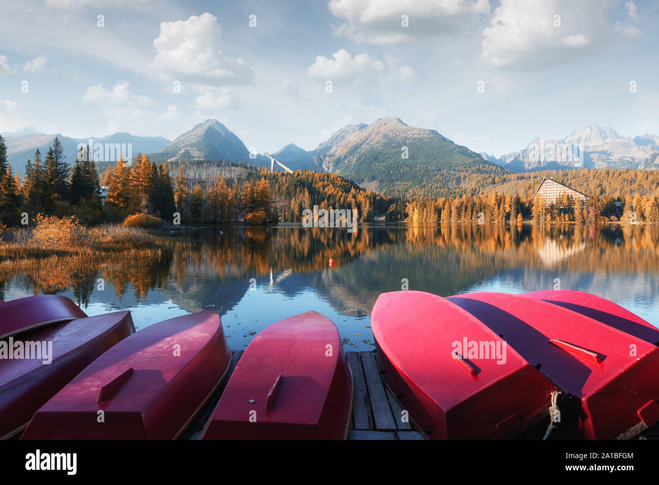Il pittoresco paesaggio autunnale con fila di rosso le barche in legno e le alte montagne sullo sfondo. Il villaggio di Strbske Pleso lago in Alti Tatra National Park, Slovacchia Foto Stock