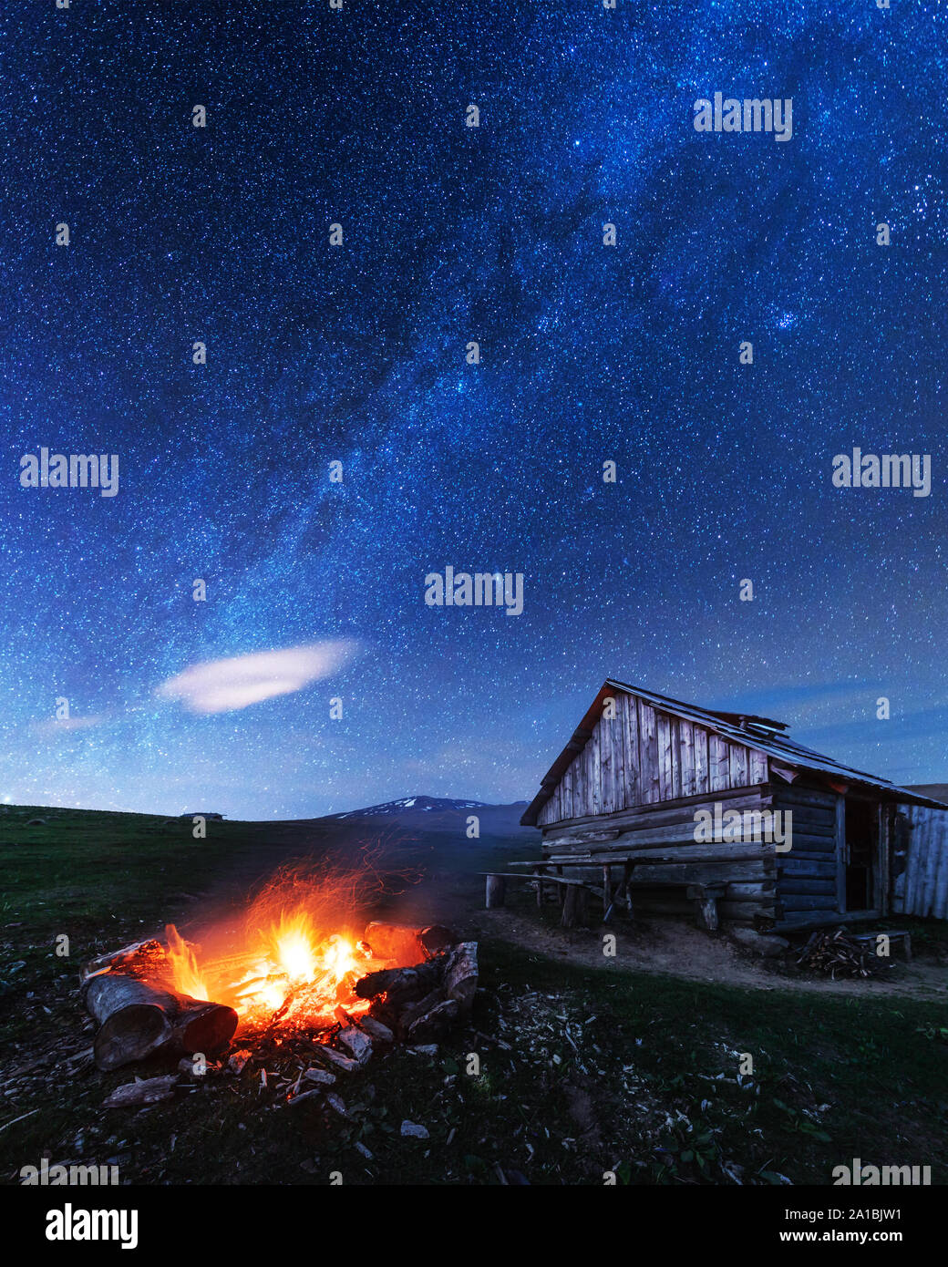 Campfire vicino alla vecchia casa in legno su strarry notte sullo sfondo del cielo Foto Stock